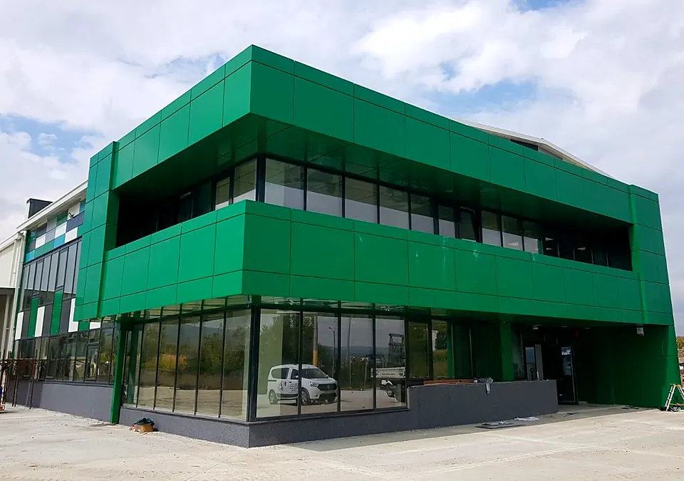 Clădire de birouri cu volum în consolă placat cu bond verde și parter vitrat din aluminiu și sticlă
