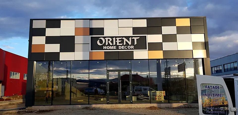 Showroom cu fascia placată cu casete din bond în mozaic negru, alb, gri și cupru, deasupra unei vitrine din sticlă pe toată lungimea